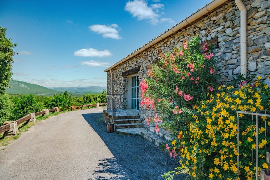 Bâtiment de pierre bordé de lauriers-roses, ouvert sur la vallée